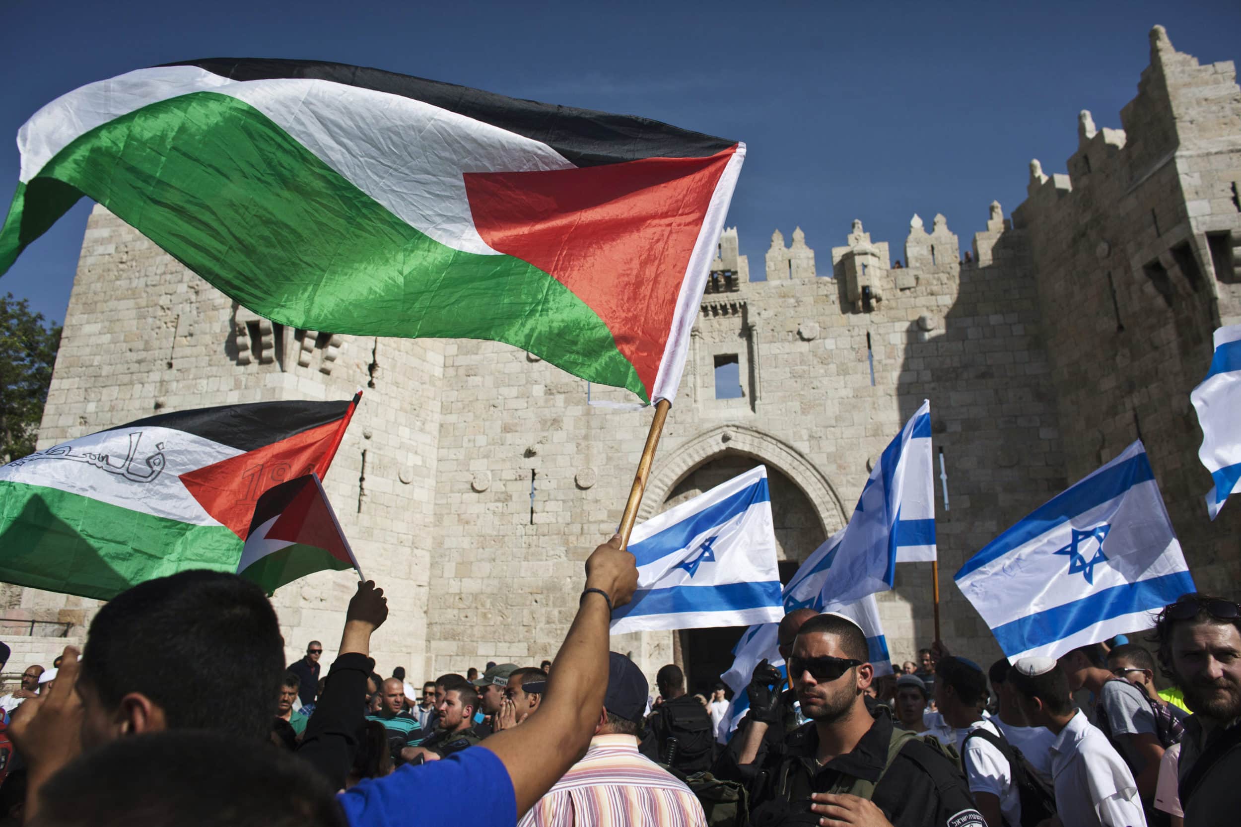 Palestinian protesters wave Palestinian flags as Israelis carrying Israeli flags walk past outside Jerusalem's Old City during a parade marking Jerusalem Day
