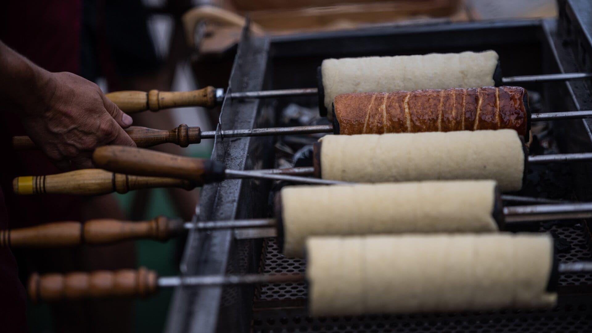 Kürtőskalács being prepared over charcoal.