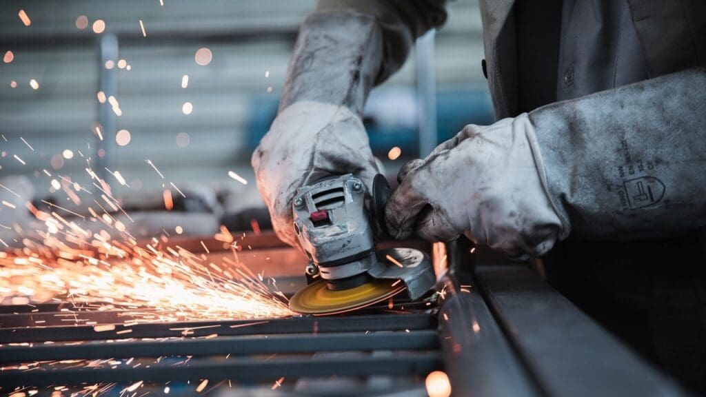 Worker hands in protective gloves grinding with electric wheel on metal.