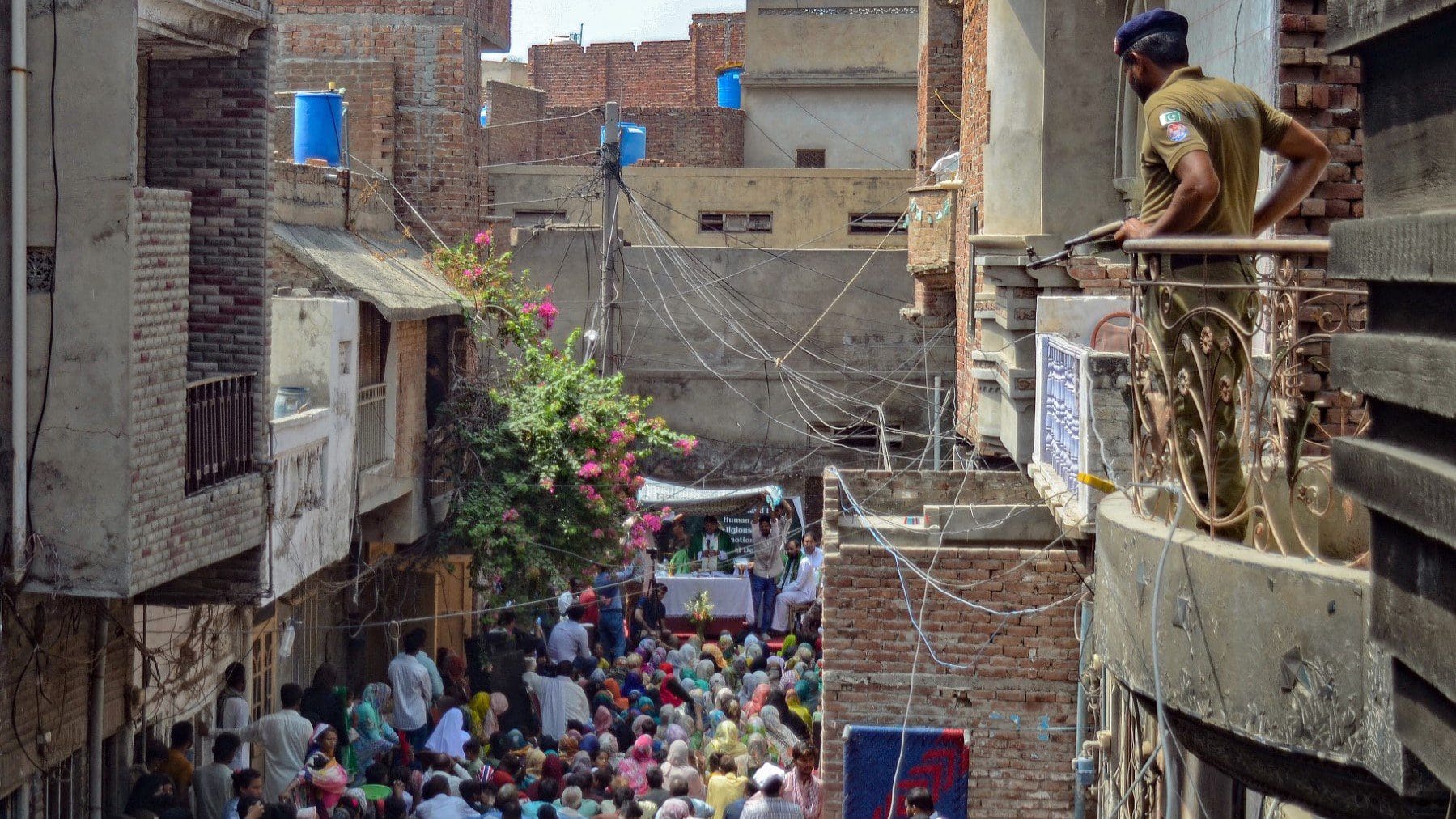 A policeman stands guard as Christians attend a Sunday Service near the torched Saint John Church in Jaranwala on the outskirts of Faisalabad on August 20, 2023, after mob attacked several Pakistani churches over blasphemy allegations. A Muslim cleric is among a dozen people being investigated for using mosque loudspeakers to order protests against alleged blasphemy by Christians which erupted into mob violence in Pakistan earlier this week, a senior police official said. More than 80 Christian homes and 19 churches were vandalised when hundreds rampaged through a Christian neighbourhood in Jaranwala in Punjab province on August 16. (Photo by Ghazanfar MAJID / AFP)