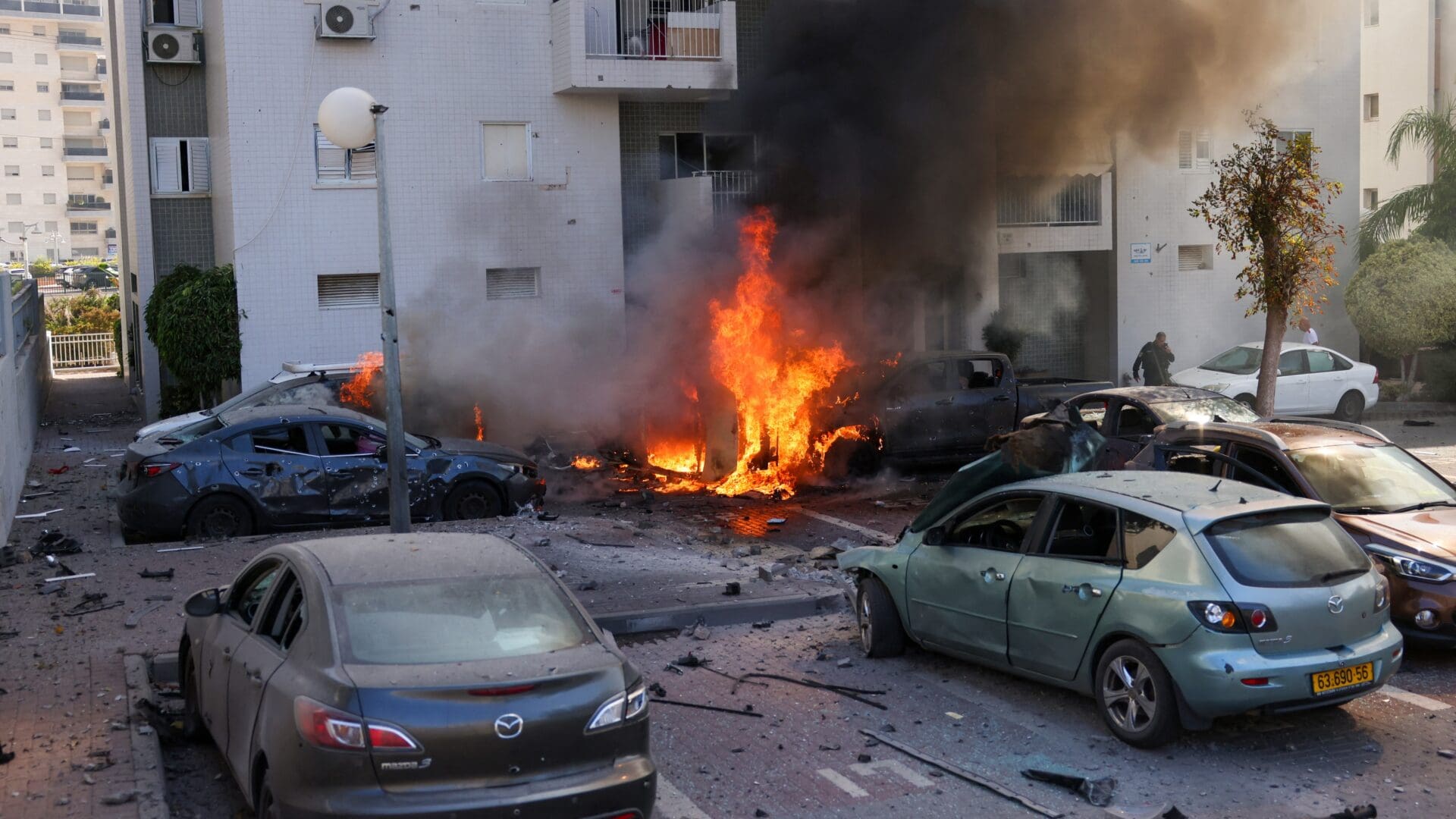 A member of the Israeli security forces stands near burning cars following a rocket attack from the Gaza Strip in Ashkelon, southern Israel, on 7 October 2023.