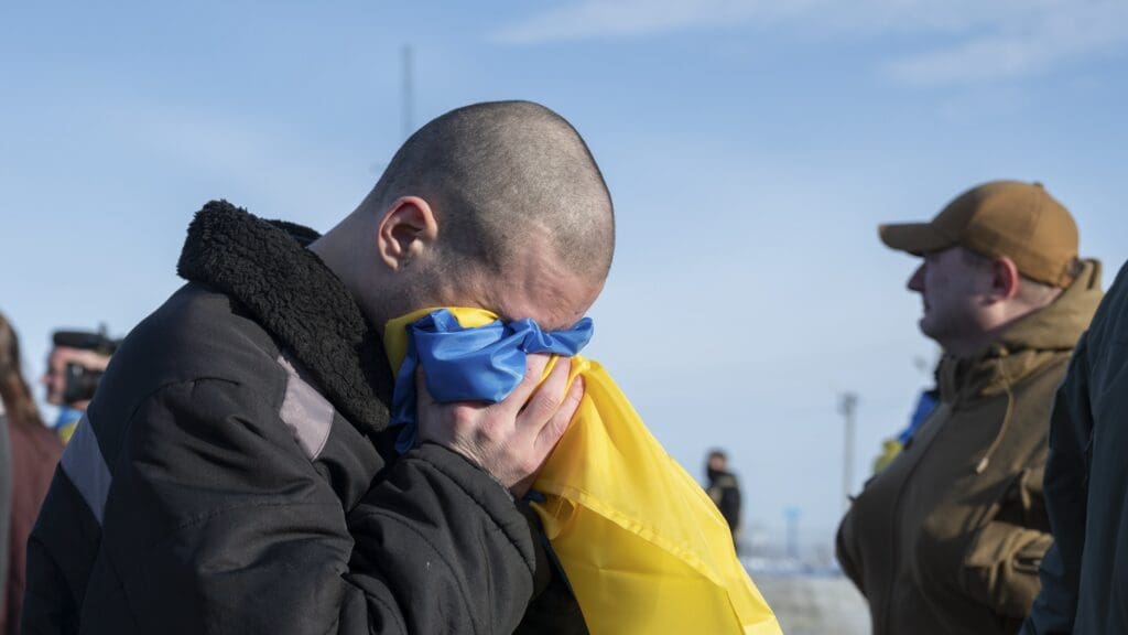 A Ukrainian soldier released from Russian captivity buries his face in a national flag after arriving on Ukrainian territory on 31 January 2024.