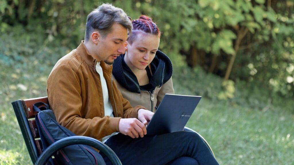 Young couple looking at the screen of a laptop in a park.