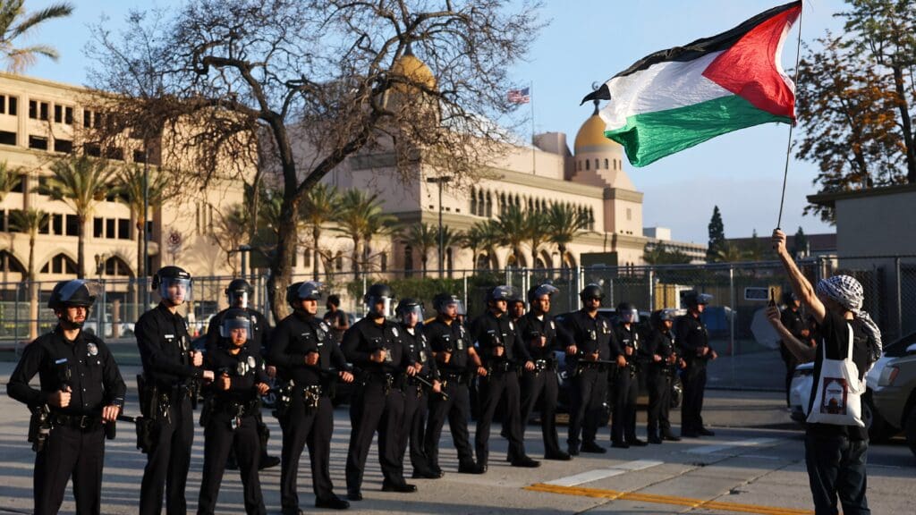 A pro-Palestinian protestor holds a Palestinian flag near a line of LAPD officers outside Pomona College's commencement ceremony at Shrine Auditorium on 12 May 2024 in Los Angeles, California.
