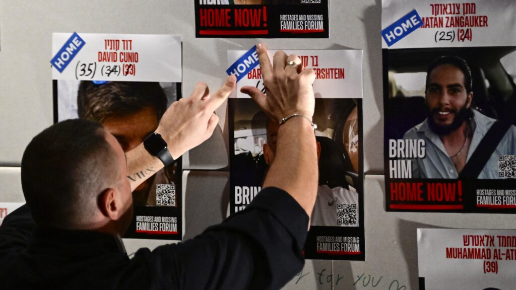 A man fixes a sticker reading 'home' on a poster showing one of the recently released hostages, on the sidelines of the Nova Music Festival Exhibition dedicated to the victims of the October 7, 2023 attack on the Supernova Sukkot Gathering in Israel, in Berlin, on October 14, 2025, one day after Israel and Hamas started to exchange hostages and prisoners.