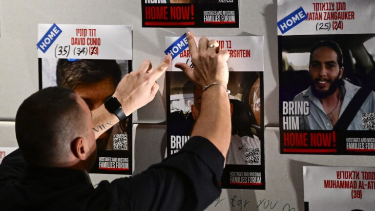 A man fixes a sticker reading 'home' on a poster showing one of the recently released hostages, on the sidelines of the Nova Music Festival Exhibition dedicated to the victims of the October 7, 2023 attack on the Supernova Sukkot Gathering in Israel, in Berlin, on October 14, 2025, one day after Israel and Hamas started to exchange hostages and prisoners.