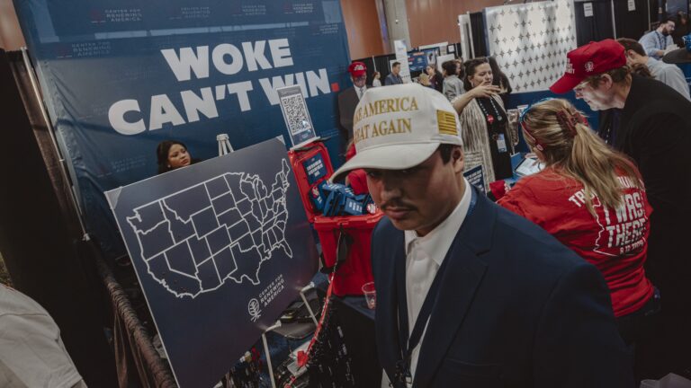 Attendees walk past a banner reading "woke can't win" as they wait for the start of Turning Point's annual AmericaFest conference, in remembrance of late right-wing political activist Charlie Kirk, in Phoenix, Arizona on December 18, 2025.