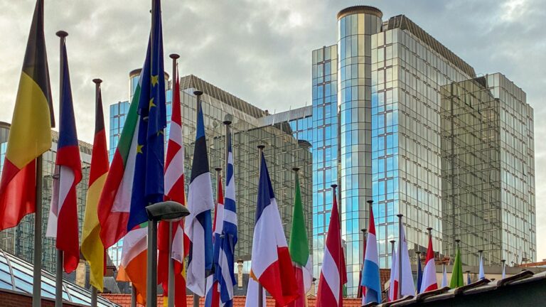A row of European Union member state flags flies in front of the glass-facade building of the European Parliament in the European Quarter in Brussels, Belgium, on December 16, 2025.