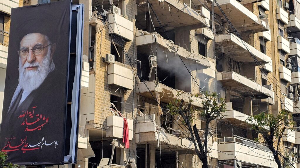 banner of Iran’s supreme leader Ayatollah Ali Khamenei is seen next to a building damaged by an Israeli strike in the southern suburbs of Beirut on March 3, 2026.